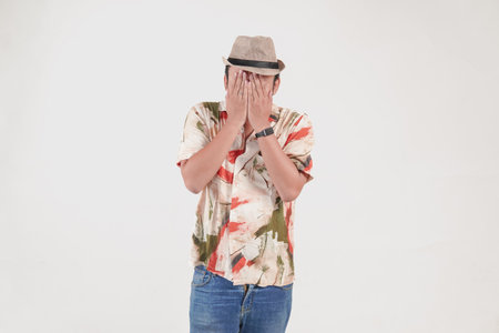 Terrified young Asian tourist man covering his eyes feeling scared isolated by white background....