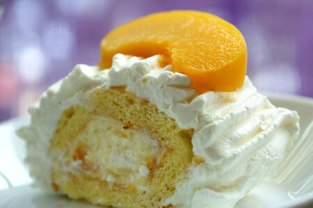 Vanilla and cream cake with a peach slice on topの写真素材