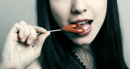 Portrait of the young brunette with a sweet in the form of heart. の写真素材