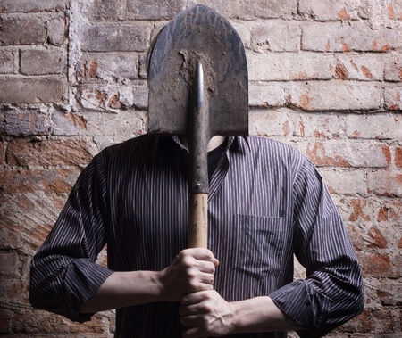 A man hides his face behind a shovel. Depersonalization, a metaphor.の写真素材