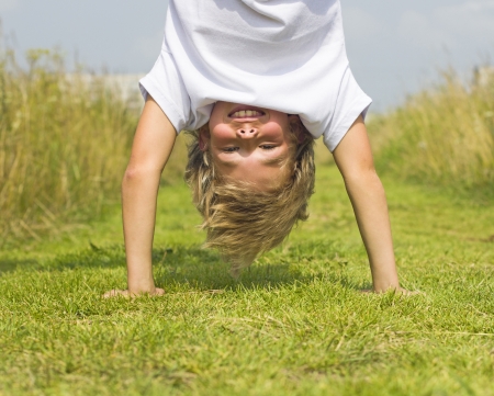 A boy stands upside down in the summer grass の写真素材