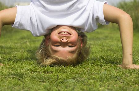 A boy stands upside down in the summer grass の写真素材