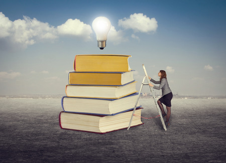 Businesswoman climbing the stairs to the foot of books for new ideas.の写真素材