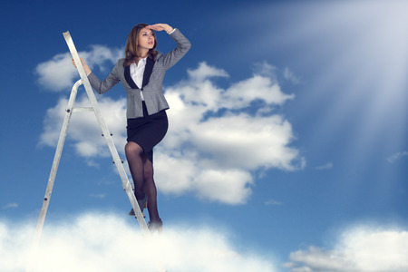 Businesswoman climbing the stairs to the sky looking into the distance.の写真素材