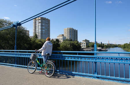 A woman with a bicycle standing on the bridge admires the view of the Tsna and Tambov river on a summer dayの写真素材