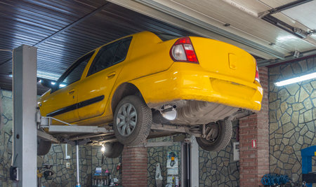 Yellow car hanging on a lift in an auto repair shop, close-upの写真素材