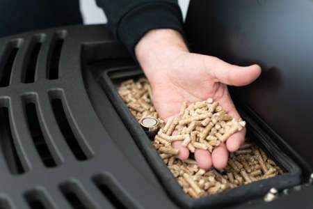Pellet stove, man holding pellets in his hand above a modern black stoveの写真素材