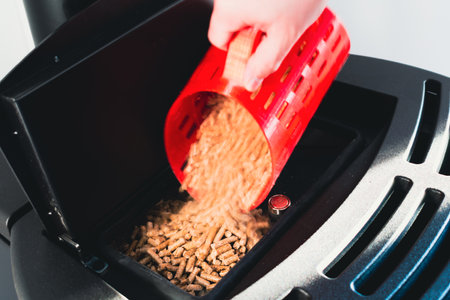 Close-up on pellets, black domestic pellet stove, man loading by hand pellets with a red 3 d printed cupの写真素材