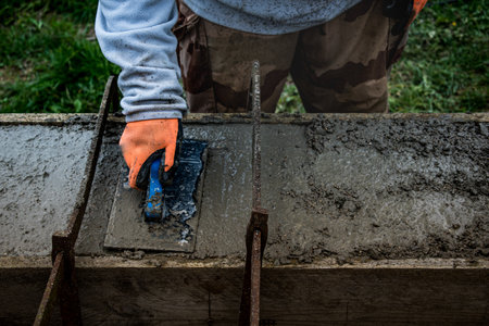 Bricklayer spreading concrete with a trowel and level to build a wall at a construction siteの写真素材