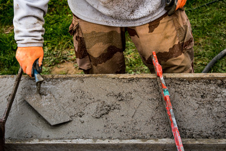 Bricklayer spreading concrete with a trowel and level to build a wall at a construction siteの写真素材