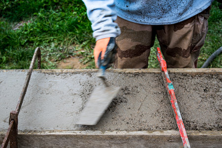 Bricklayer spreading concrete with a trowel and level to build a wall at a construction siteの写真素材