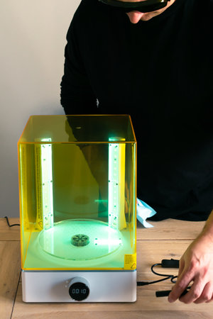 Man wearing glasses adjusting a wash and cure machine using UV light before use, for 3d resin...