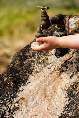 Baby cleaning his hands at an outdoor tap coming out of a stone, refreshing splashes without wasting...
