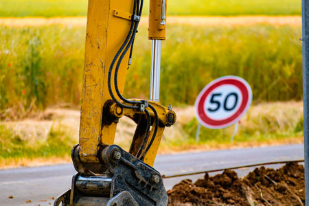 Arm of a mini digger and bucket with a speed limit sign at 50, road signの写真素材