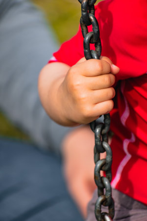 Close-up on a baby's hand holding a chain, kid having fun playing on a swingの写真素材
