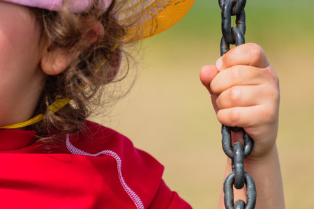Close-up on a baby's hand holding a chain, kid having fun playing on a swingの写真素材
