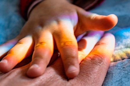 Baby's hand on a mother's hand with a rainbowの写真素材