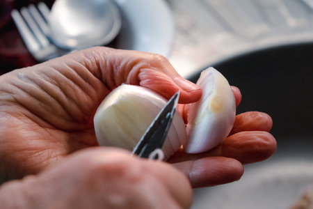 Hand peeling and cutting a red onion in a kitchen