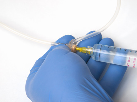 The hand in a blue glove lifts a tube of system with a syringe, ntroduction of medicine to transfusion systemの写真素材
