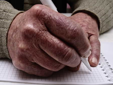 Closeup of the wrinkled hands of an old caucasian man holding pen and paper, wearing a green sweaterの写真素材