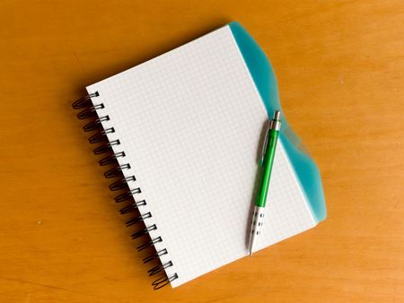 Photo of the spiral notebook with pen over wooden background.