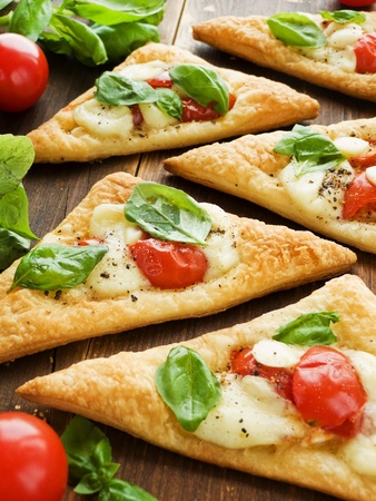 Puff-pizzas with mozzarella cheese, cherry tomatoes and baby basil. Shallow dof.の写真素材