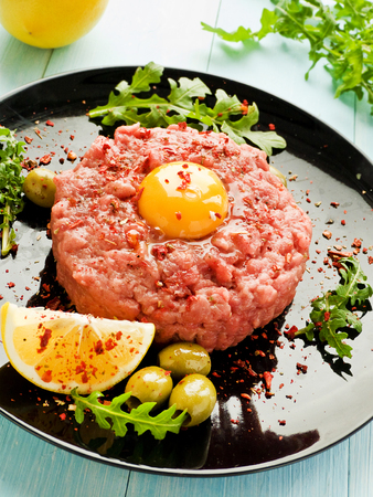 Plate with raw beef tartar with olives, lemon and herbs. Shallow dof.の写真素材