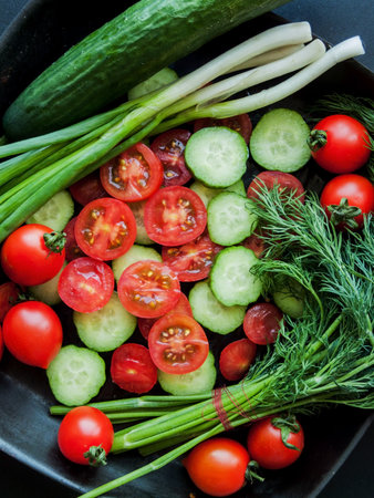 Seasonal diet and nutrition, healthy eating concept. Fresh red cherry tomatoes, green leek and cucumber in pan on the black background, top view of vegetables covered with water drops.の写真素材