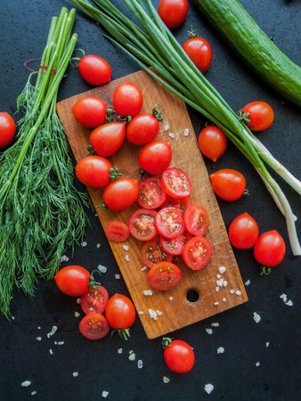Seasonal diet and nutrition, healthy eating concept. Fresh red cherry tomatoes with herbs and leek sprinkled with sea salt on the wooden board on the table, top view of vegetables covered with drops.の写真素材