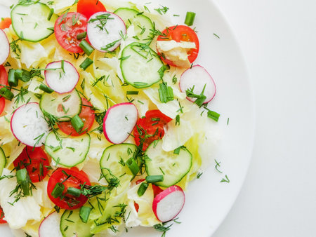 Home cooking and healthy eating concept. Plate with fresh spring salad of sliced radish, cherry tomatoes, cucumber, greens and iceberg salad covered in olive oil, top view of plate with vitamin meal.の写真素材