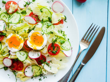 Home cooking and healthy eating concept. Plate with fresh spring salad of radish, cherry tomatoes, cucumber, greens iceberg and boiled eggs salad in olive oil, top view of plate with vitamin meal.の写真素材