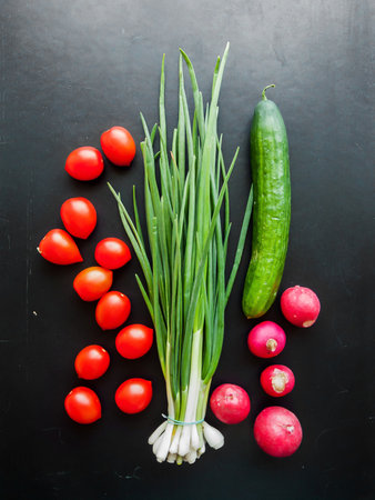 Seasonal diet and nutrition, healthy eating concept. Bunch of fresh red cherry tomatoes, green leek, radish and cucumber on the black table background, top view of vegetables on the table.の写真素材