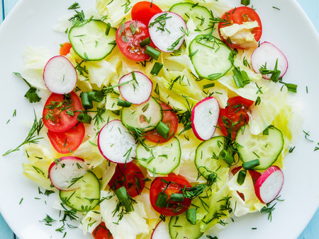 Home cooking and healthy eating concept. Plate with fresh spring salad of sliced radish, cherry tomatoes, cucumber, greens and iceberg salad covered in olive oil, top view of plate with vitamin meal.の写真素材