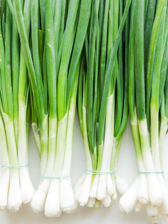 Seasonal diet and nutrition, healthy eating concept. Fresh green leek onion on the white wooden background, top view bunch of greens on the table.の写真素材