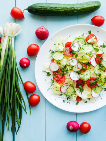 Home cooking and healthy eating concept. Plate with fresh spring salad of sliced radish, cherry tomatoes, cucumber, greens and iceberg salad covered in olive oil, top view of plate with vitamin meal.の写真素材