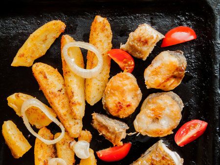 Cooking and healthy eating concept. Oven pan with sliced baked potatoes, fish steaks and vegetables with onion on the table. Homemade healthy dinner with potatoes and seafood.の写真素材
