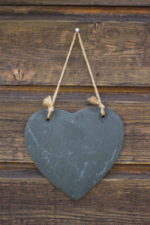 black heart hanging infront of wooden wallの写真素材