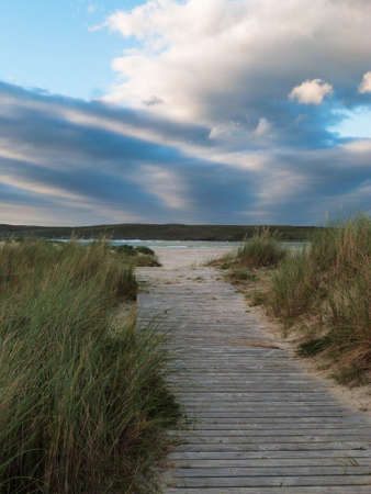 wooden pathway through dunes to the ocean an cloudy sky in irelandの写真素材