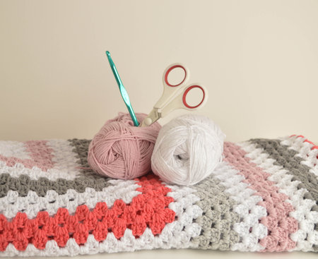 woolen balls with crochet granny square blanket in basket and crochet hook and scissors