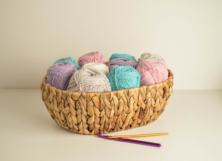 pastel colored woolen balls in a basket with crochet hooks for crocheting and handicraft