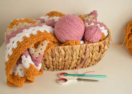 soft colored woolen balls with granny square blanket and crochet hook in basket