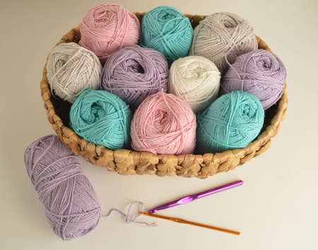 pastel woolen balls in basket with crochet hooks