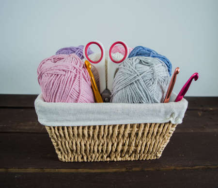 pastel colored woolen balls in basket with scissors and crochet hook on dark brown wooden ground handmadeの写真素材
