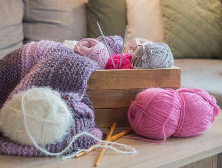 Colorful woolen balls in a wooden box with knitting needles and a white knitted scarf handmade
