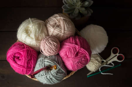 Colorful woolen balls with crochet hooks in a wooden basket in front of a dark brown wooden...