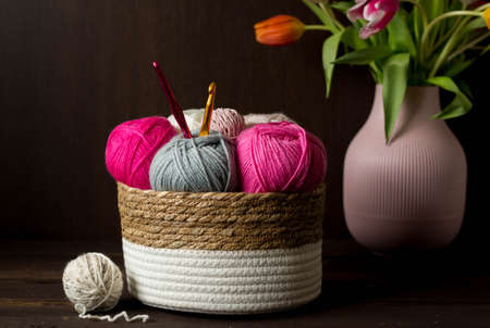Colorful woolen balls with crochet hooks in a wooden basket in front of a dark brown wooden background handmadeの写真素材