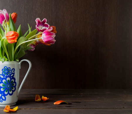 pink and orange colored tulips in vase in front of a dark brown wooden wall backgroundの写真素材