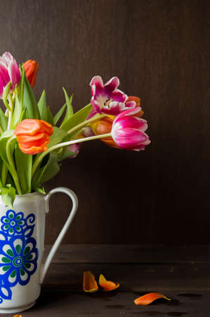 pink and orange colored tulips in vase in front of a dark brown wooden wall backgroundの写真素材
