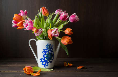 pink and orange colored tulips in vase in front of a dark brown wooden wall backgroundの写真素材