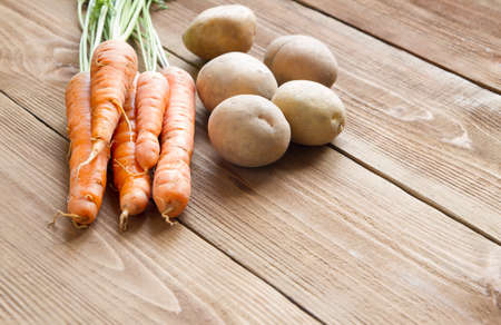 Fresh carrots and potatoes on a light wooden backgroundの写真素材